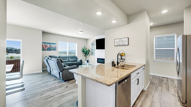 A modern kitchen with a granite countertop, stainless steel appliances, and a dining area with a gray sofa. - The Hills in Lorson Ranch (Colorado Springs)