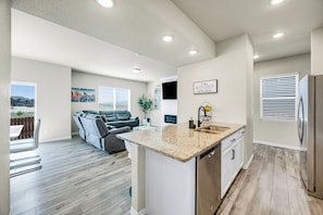 A modern kitchen with a granite countertop, stainless steel appliances, and a dining area with a gray sofa.