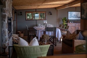 Un comedor con chimenea de piedra, techo de madera y una mesa dispuesta para una comida.