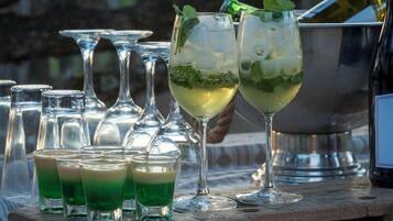 Un bar con vasos de una bebida verde, una botella y un recipiente metálico.