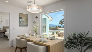 Un comedor moderno con una mesa de madera, dos sillas, un jarrón con flores y vista al mar.