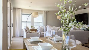 Una sala moderna con comedor, un conjunto de sofás, un televisor y un jarrón con flores.