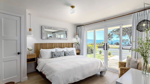 Un dormitorio con cama, mesita de noche, espejo, ventana con vistas y puerta.