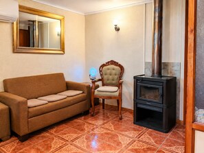 A living room with a sofa, a chair, a wall-mounted mirror, a wall sconce, and a wood-burning stove.