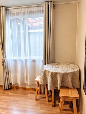 A room with a round table and bench, a window with sheer curtains, and a view of a building outside.