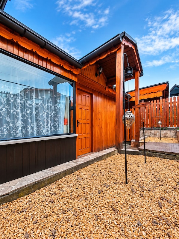 A wooden house with a large window, a wooden door, and a gravel driveway.
