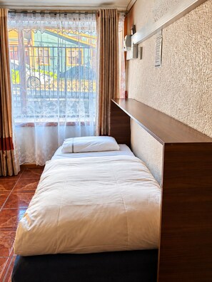 A hotel room with a bed, a wooden headboard, a window with curtains, and a view of the outside.