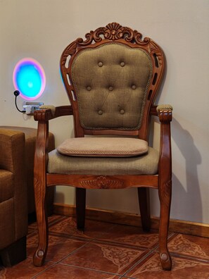 A wooden chair with a cushioned seat and backrest, positioned in a room with patterned floor tiles.