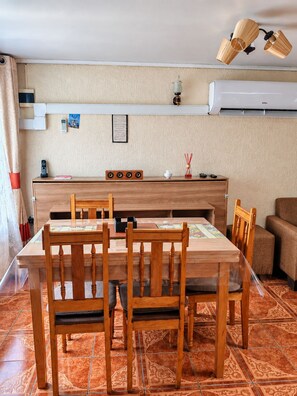 A dining area with a wooden table and chairs, a kitchen counter with a sink, and an air conditioning unit above.