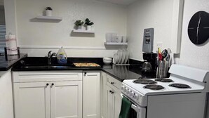 Una cocina con armarios blancos, estufa, lavabo y cafetera.