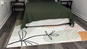 Un dormitorio con una cama, dos mesitas de noche, una lámpara y una alfombra.