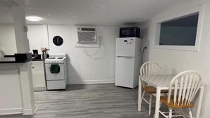 Cocina compacta con lavadora, microondas y refrigerador. Hay dos sillas blancas junto a una mesa pequeña.