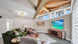 Ein modernes Wohnzimmer mit einem großen Fernseher, einem grünen Sofa und einer Holzbalkendecke.