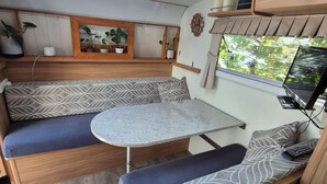 A compact RV interior with a kitchenette, a dining area, and a seating area with cushions. - Quirky & Comfortable: A 'Tiny Home' Experience in a great spot (Heidelberg)