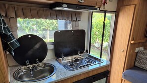 A compact kitchenette with a gas stove, sink, and a window with a view of greenery. - Quirky & Comfortable: A 'Tiny Home' Experience in a great spot (Heidelberg)