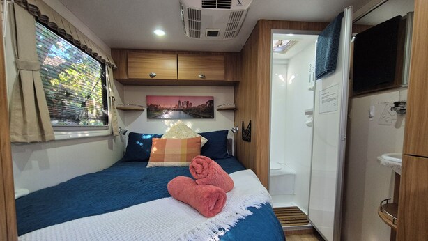 A bedroom with a bed, a window with curtains, a wall-mounted air conditioner, a painting, and a bathroom with a sink and mirror. - Quirky & Comfortable: A 'Tiny Home' Experience in a great spot (Heidelberg)