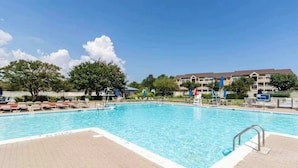 A swimming pool with a tiled deck, lounge chairs, and a building in the background. - Bay Watch 1 203A, Outdoor Pool, Beautiful Condo (Ocean City)