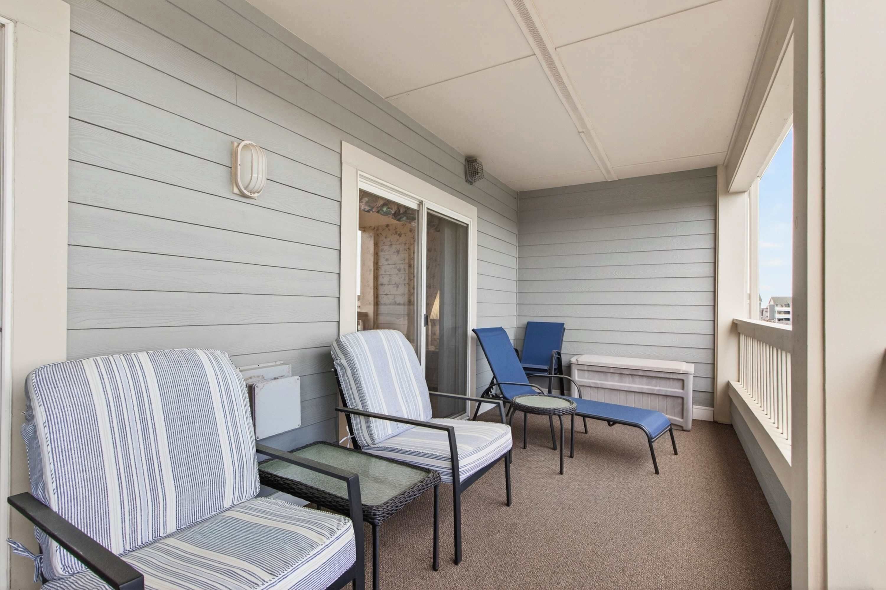 Een overdekt balkon met een rij stoelen en een bankje, een witte balustrade, en uitzicht op de stad.