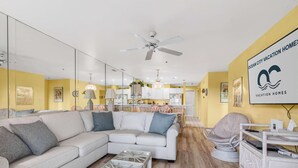 A modern living room with a sofa, coffee table, and a dining area in the background. - Bay Watch 1 203A, Outdoor Pool, Beautiful Condo (Ocean City)