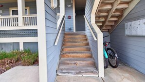 A wooden staircase leading to a building entrance, a bicycle parked outside, and a mailbox on the wall. - Bay Watch 1 203A, Outdoor Pool, Beautiful Condo (Ocean City)