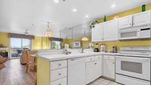 A modern kitchen with white cabinets, a microwave, and a stove. There is a dining area with a chair and a table. - Bay Watch 1 203A, Outdoor Pool, Beautiful Condo (Ocean City)