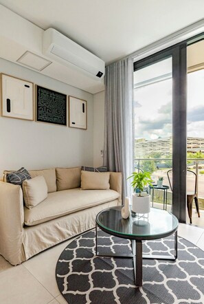 Un salon moderne avec un canapé beige, une table basse en verre et une vue sur le paysage urbain, visible à travers de grandes fenêtres.