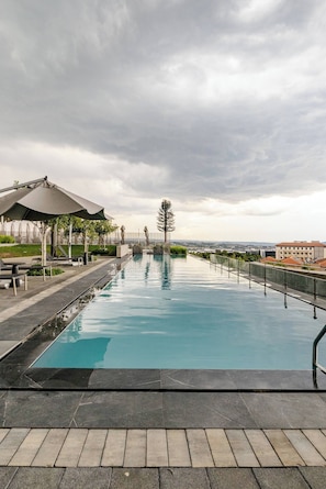 A swimming pool with a paved walkway, lounge chairs, and a covered seating area.