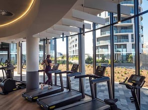 A modern gym with treadmills, a woman exercising, large windows, and a view of a building.