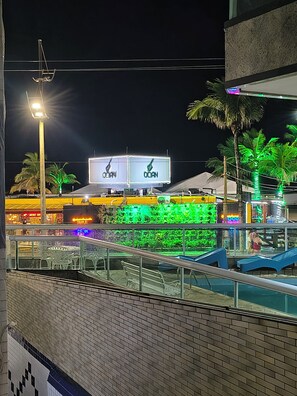 Een nachtzicht van een waterkant met verlichte reclameborden, palmbomen en een gevel van een bakstenen gebouw.