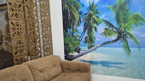 A tan sofa in a room with a large tropical mural, a wooden decorative partition, and a tiled floor. - Beachfront apartment in Praia Grande, right on the sand. (Praia Grande)