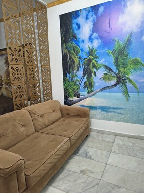 Um sofá bege em um quarto com um grande mural tropical, um painel decorativo de madeira e piso de azulejos.