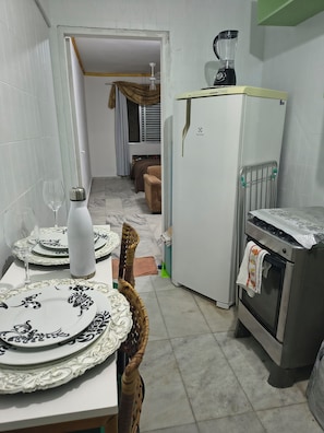 A compact kitchen with a refrigerator, oven, and a blender on top. There is a dining table with plates and a wine glass. - Beachfront apartment in Praia Grande, right on the sand. (Praia Grande)