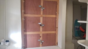 A room with a wooden door, a white wall, a white shelf, and a blue fan. - Roseau Beach Hostel  (Roseau)