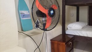 A bunk bed with a wooden headboard, a small wooden nightstand, and a standing fan with a red and black design. - Roseau Beach Hostel  (Roseau)