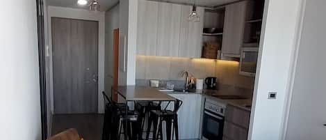 A modern kitchen with white cabinets, a dining area with a wooden table and chairs, and a hanging pendant light.