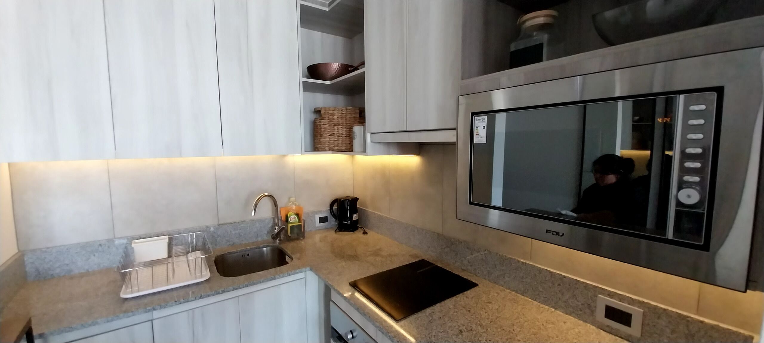A modern kitchen with a built-in microwave, a kettle, and a sink.