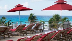 Eine Strandlounge mit Liegestühlen und roten Sonnenschirmen mit Blick auf das Meer.