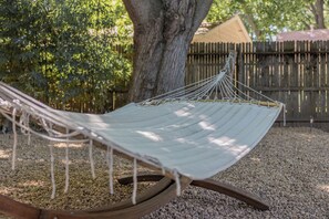 A hammock tied to a wooden stand in a garden with gravel ground, surrounded by trees and a wooden fence. - Chico Charmer ~Near Chico State University & Downtown Chico-Pet Friendly (Chico)