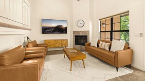 Ein Wohnzimmer mit Sofa, Couchtisch, Fernseher, Kamin und einer Wanduhr.