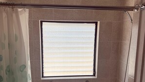 Un baño con bañera, una ventana con persianas, zona de ducha y barra de apoyo.