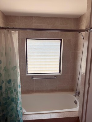 A bathroom with a bathtub, a window with blinds, a shower area, and a handrail. - Suite in Zone 10 : Exclusive and secure location (Ciudad de Guatemala)