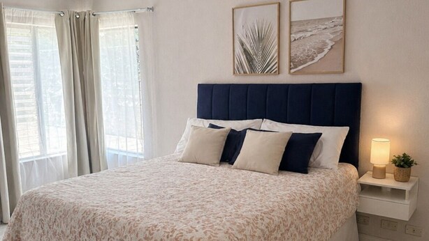 Un dormitorio con una cama grande, una mesita de noche con lámpara y dos cuadros enmarcados en la pared.