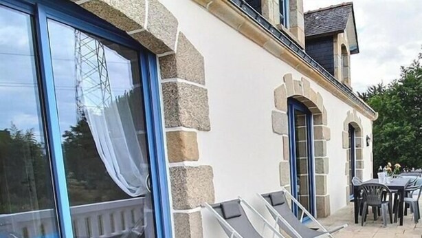 Ein Gebäude mit Steinmauern, großen Glasfenstern und einer Terrasse mit zwei Liegestühlen.