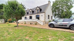 Ein zweistöckiges Haus mit einer Stein-Fassade, einer Veranda und einem parkenden Auto.