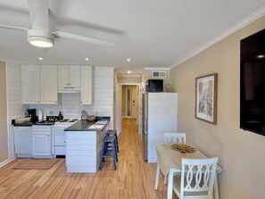 Eine kompakte Küche mit weißen Schränken, einer zentralen Kücheninsel, einem Essbereich mit Tisch und Stühlen sowie einem Deckenventilator.