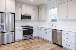 Une cuisine moderne avec des meubles blancs, des appareils en acier inoxydable et un plancher en bois.