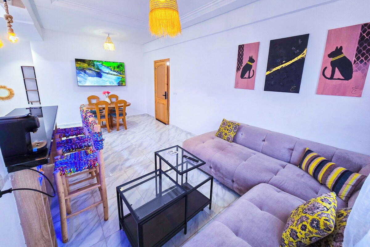 A living room with a sofa, a coffee table, a TV, and a dining area with chairs and a table.
