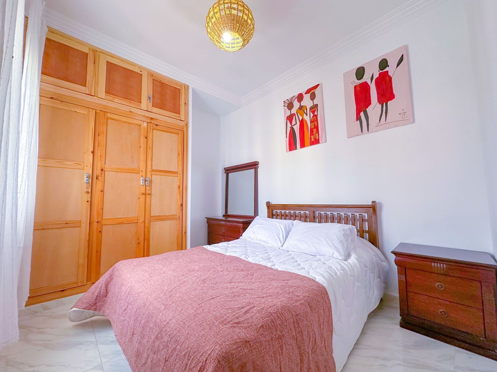 Un dormitorio con cama, armario de madera, cómoda y obras de arte en la pared.