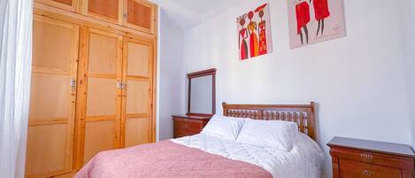 Un dormitorio con cama, armario de madera, cómoda y obras de arte en la pared.