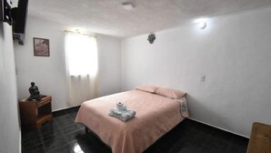 Un dormitorio con cama, mesita de noche, televisor montado en la pared y ventana con cortinas.